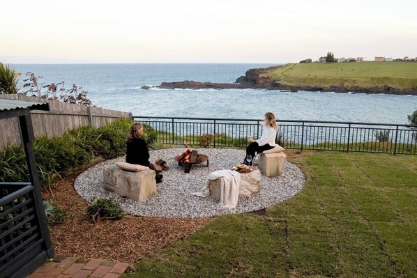 A patio with a fire pit, seating, and a view of the ocean.