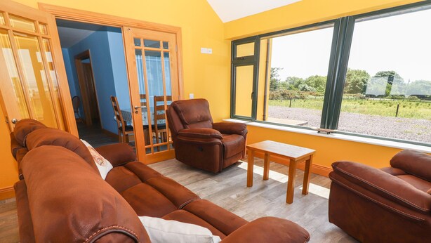 Una sala de estar con sofás de cuero, una mesa de centro de madera y vistas a un jardín a través de amplios ventanales.