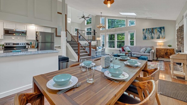 A spacious kitchen with modern appliances, a dining area with a wooden table set for four, and a cozy living room with a sofa and a fireplace.