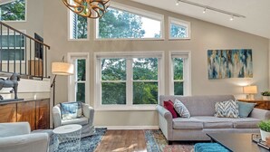 A spacious living room with a large window, a staircase, and a modern chandelier.