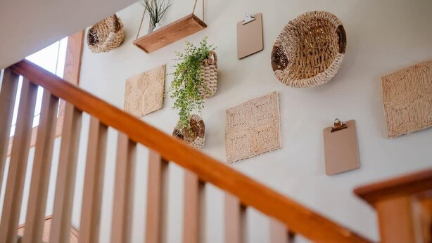 A staircase with wooden railings and a wall decorated with woven baskets and a clipboard.