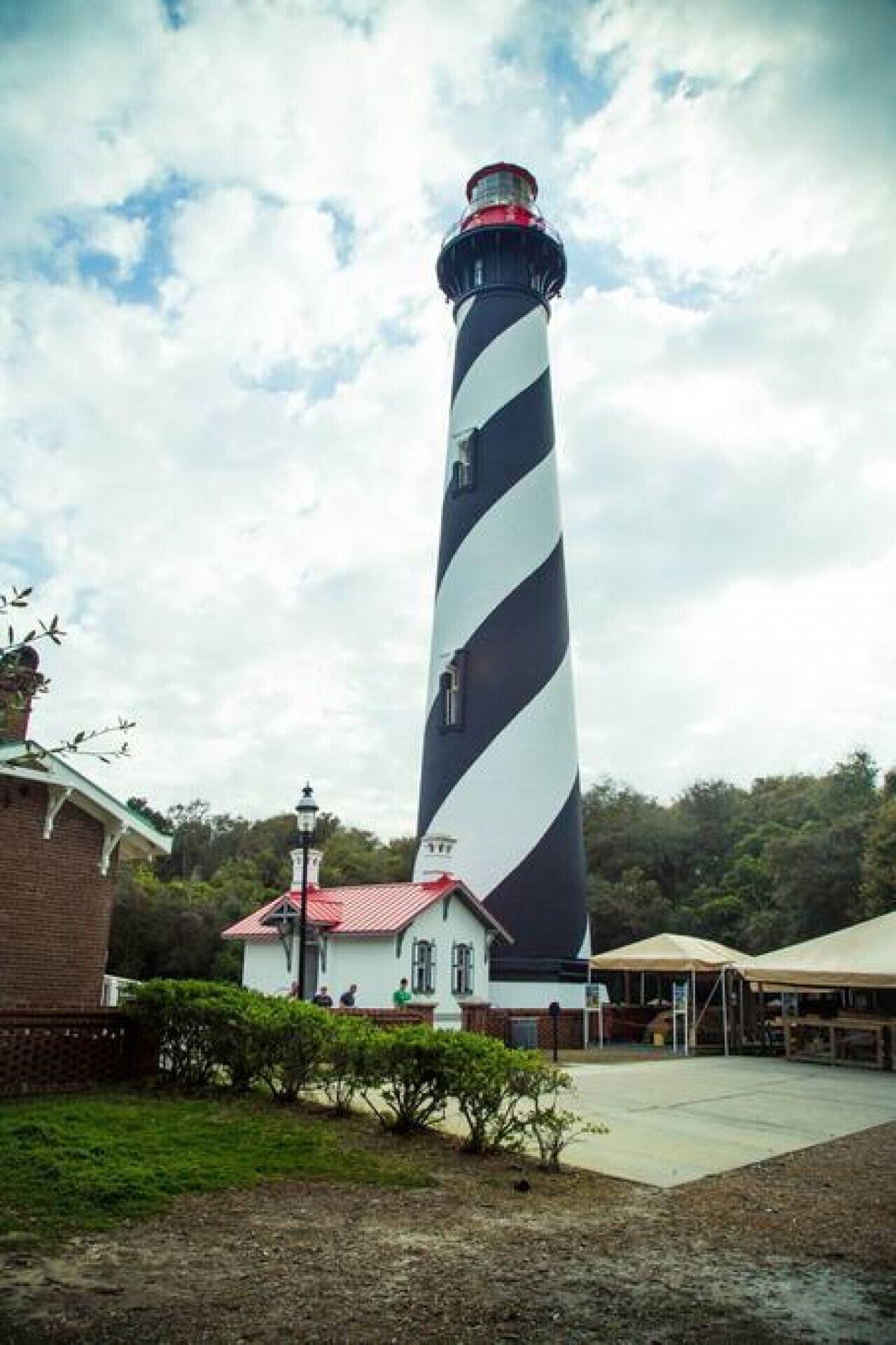 Un grand phare aux rayures noires et blanches, entouré d’un petit bâtiment doté d’un toit rouge et d’un espace abrité avec des tables.