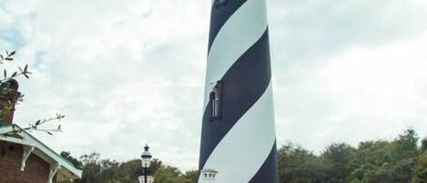 Un grand phare aux rayures noires et blanches, entouré d’un petit bâtiment doté d’un toit rouge et d’un espace abrité avec des tables.