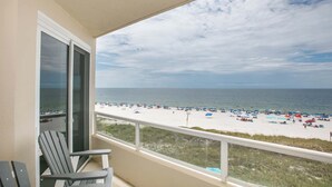 A balcony with a view of a beach, featuring a railing and two Adirondack chairs.