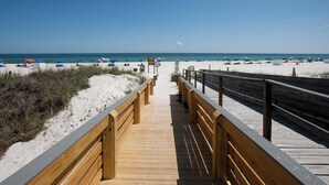 A wooden boardwalk leading to a beach with umbrellas and beach chairs.