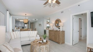 A spacious living room with a white sofa, a round coffee table, and a wooden cabinet. There is a ceiling fan and a large mirror on the wall.