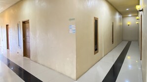 Un corridoio con pavimento a scacchi in bianco e nero, pareti beige e porte che conducono a diverse stanze.