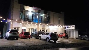 Un edificio con diverse auto parcheggiate davanti, un cartello sopra l'ingresso e una facciata ben illuminata.