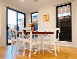 Un coin repas avec une table en bois et des chaises blanches, de grandes fenêtres offrant une vue dégagée et un tableau encadré au mur.