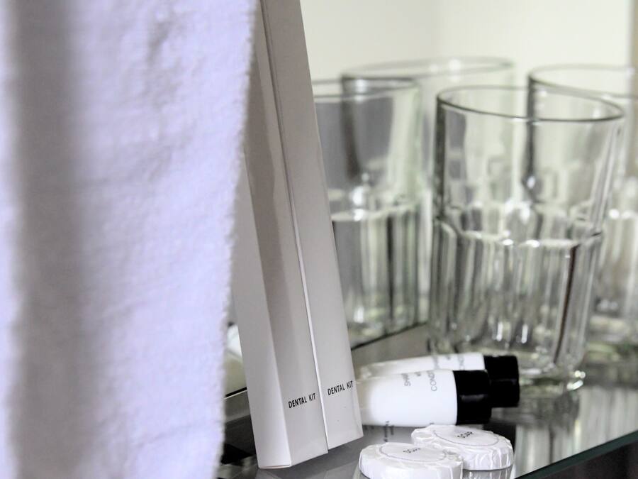 Een badkamer met een witte handdoek, een tandenborstelset en verschillende glazen bekers op een glazen plank.
