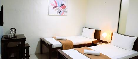Habitación de hotel con dos camas individuales, un escritorio pequeño con una silla, una mesita con una tetera y un cuadro colgado en la pared.