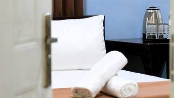 A hotel room with a neatly made bed, a wooden side table with a rolled towel, and a coffee maker on the table.