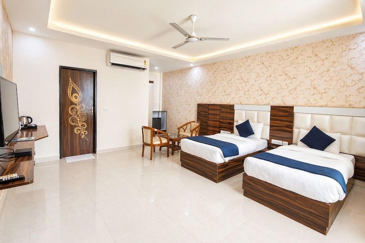 A hotel room with two beds, a desk, a chair, a television, and a ceiling fan.