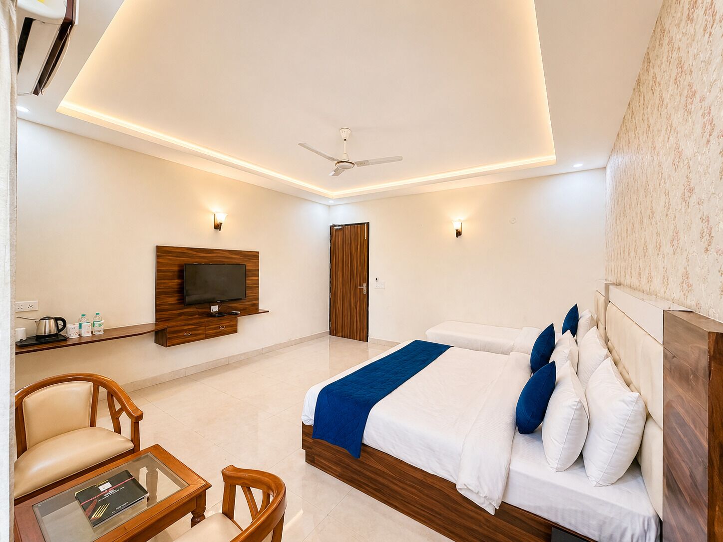 Una habitación de hotel moderna con una cama grande, un televisor montado en la pared, un ventilador de techo y un armario de madera.