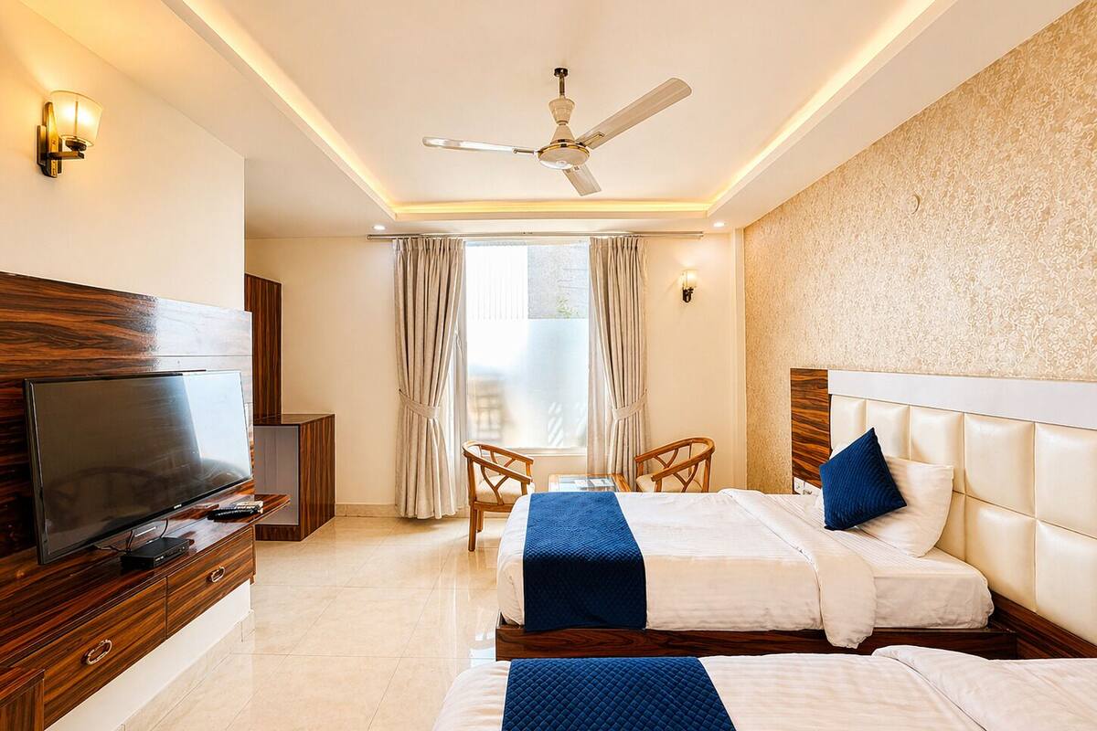 Une chambre d’hôtel équipée d’une télévision, de deux lits, d’un ventilateur de plafond et d’une fenêtre avec des rideaux.