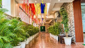 A corridor lined with potted plants, a polished floor, and a decorative ceiling with hanging floral arrangements. - Dwelling residency (Greater Noida)