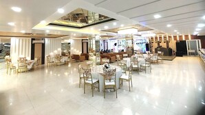 A spacious banquet hall with round tables and chairs, a stage for events, and a modern ceiling design. - Dwelling residency (Greater Noida)