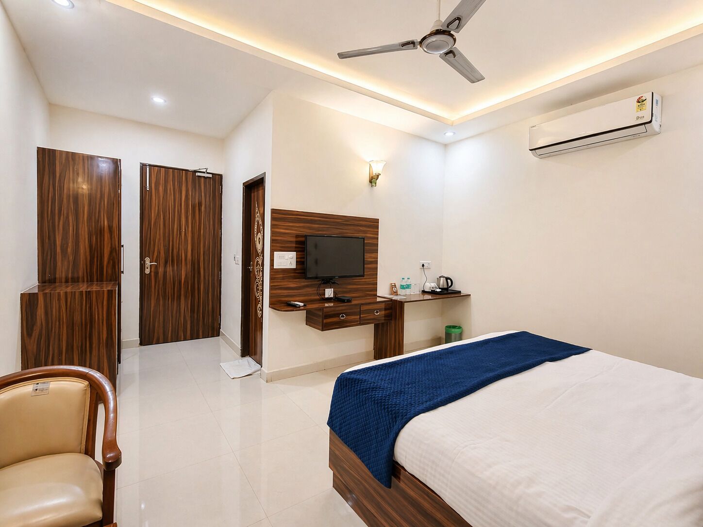 A hotel room with a bed, a desk, a television, a ceiling fan, and an air conditioning unit.