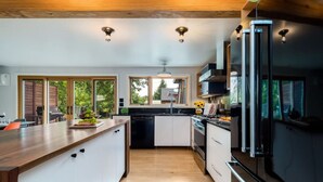 Una cocina moderna con encimera de madera, armarios blancos, un refrigerador negro y vistas al exterior a través de grandes ventanales.