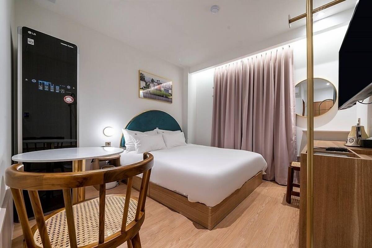 Una habitación de hotel con cama, escritorio, silla, televisor y ventana con cortinas.