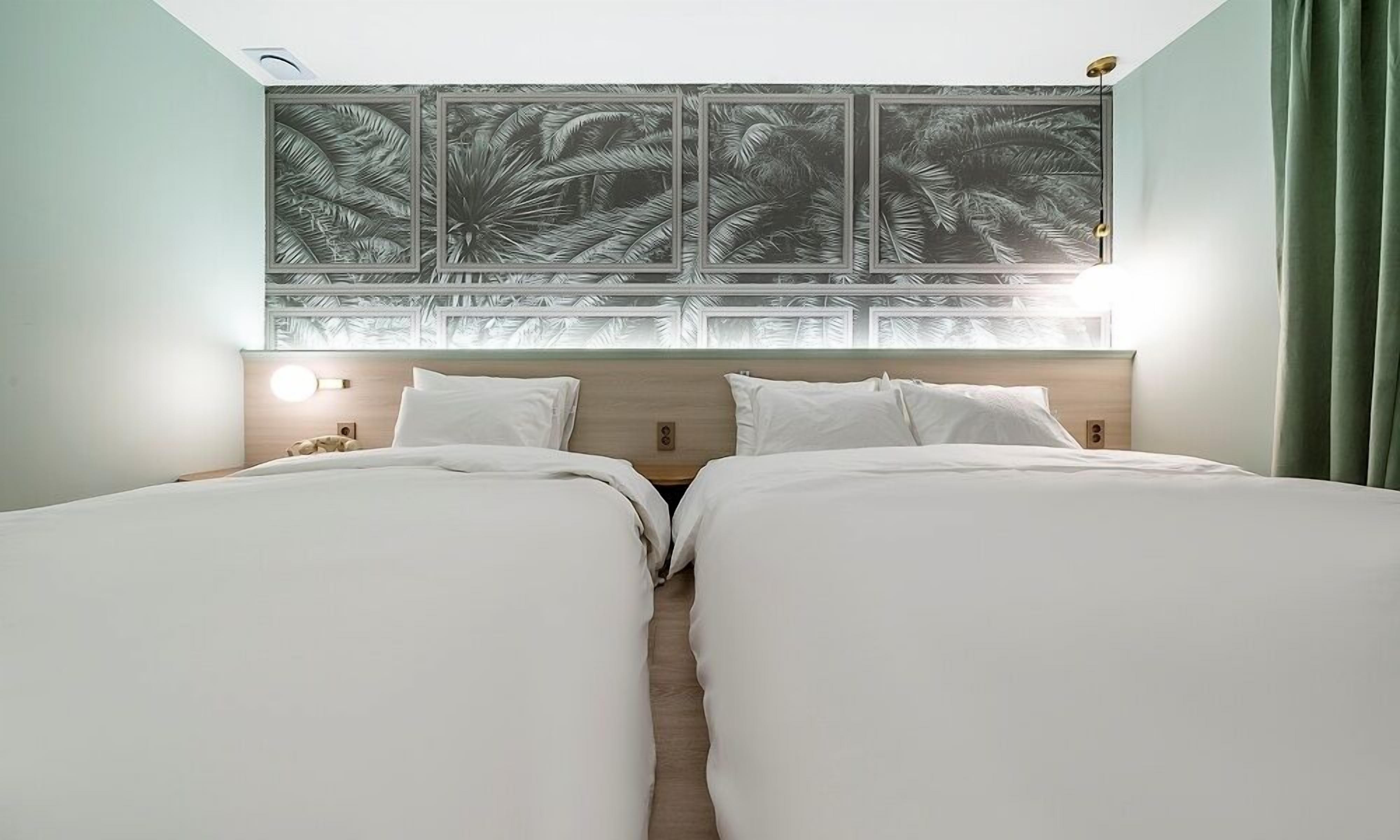 A double room with two beds, a wooden headboard, and a wall-mounted artwork of palm leaves.