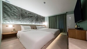 A hotel room with a large bed, a nightstand with a lamp, a television, and a wall with a tropical mural. - WONJU Hotel Ippda (Wonju)