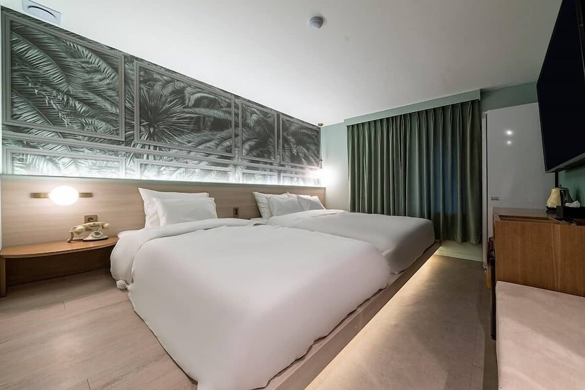 Habitación de hotel con una cama grande, una mesita de noche con lámpara, un televisor y una pared con un mural tropical.