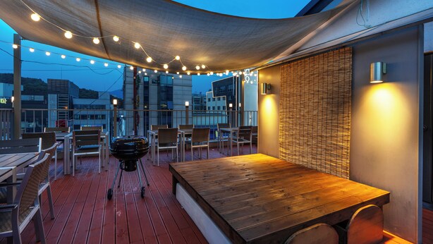 An outdoor dining area with a wooden table and chairs, string lights, and a view of the cityscape. - WONJU Hotel Ippda (Wonju)