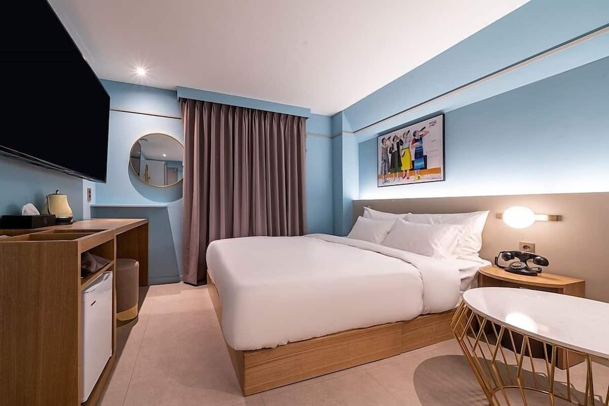 Una habitación de hotel moderna con una cama grande, un escritorio con lámpara, televisión y un cuadro en la pared.