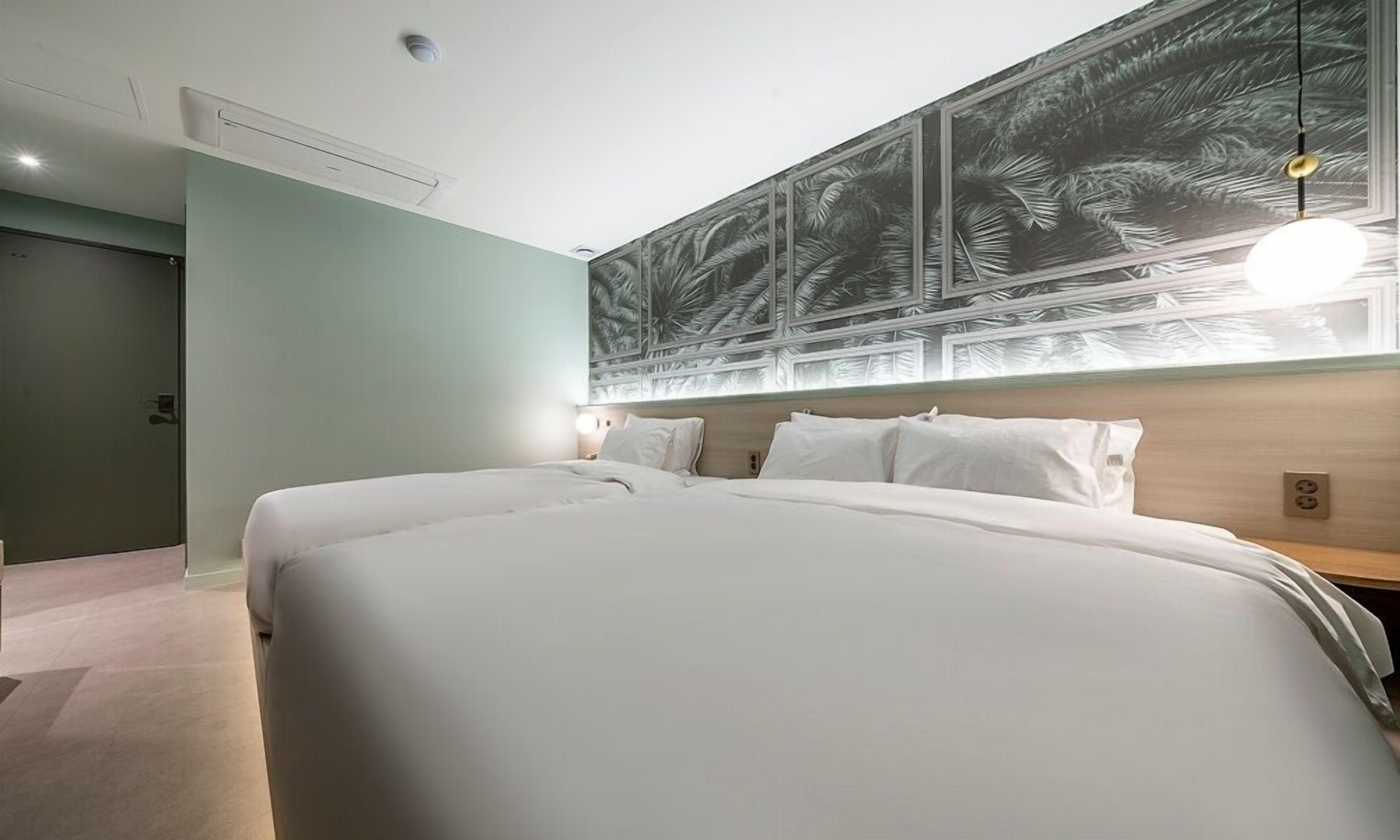 Une chambre d’hôtel moderne, dotée d’un grand lit, d’une table de chevet, d’une œuvre d’art accrochée au mur et d’une fenêtre avec des stores.