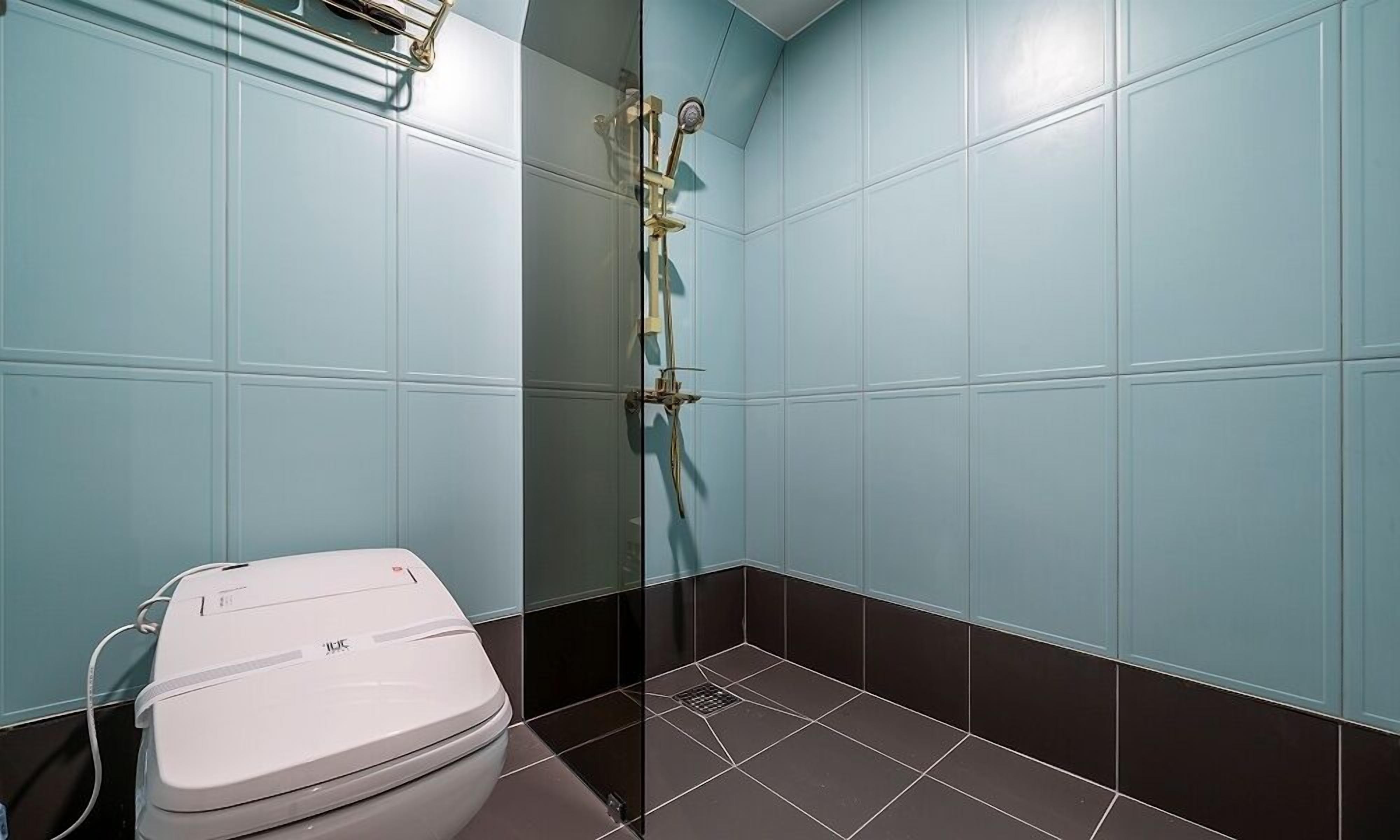 Een badkamer met toilet, douche met glazen deur en betegelde muren.