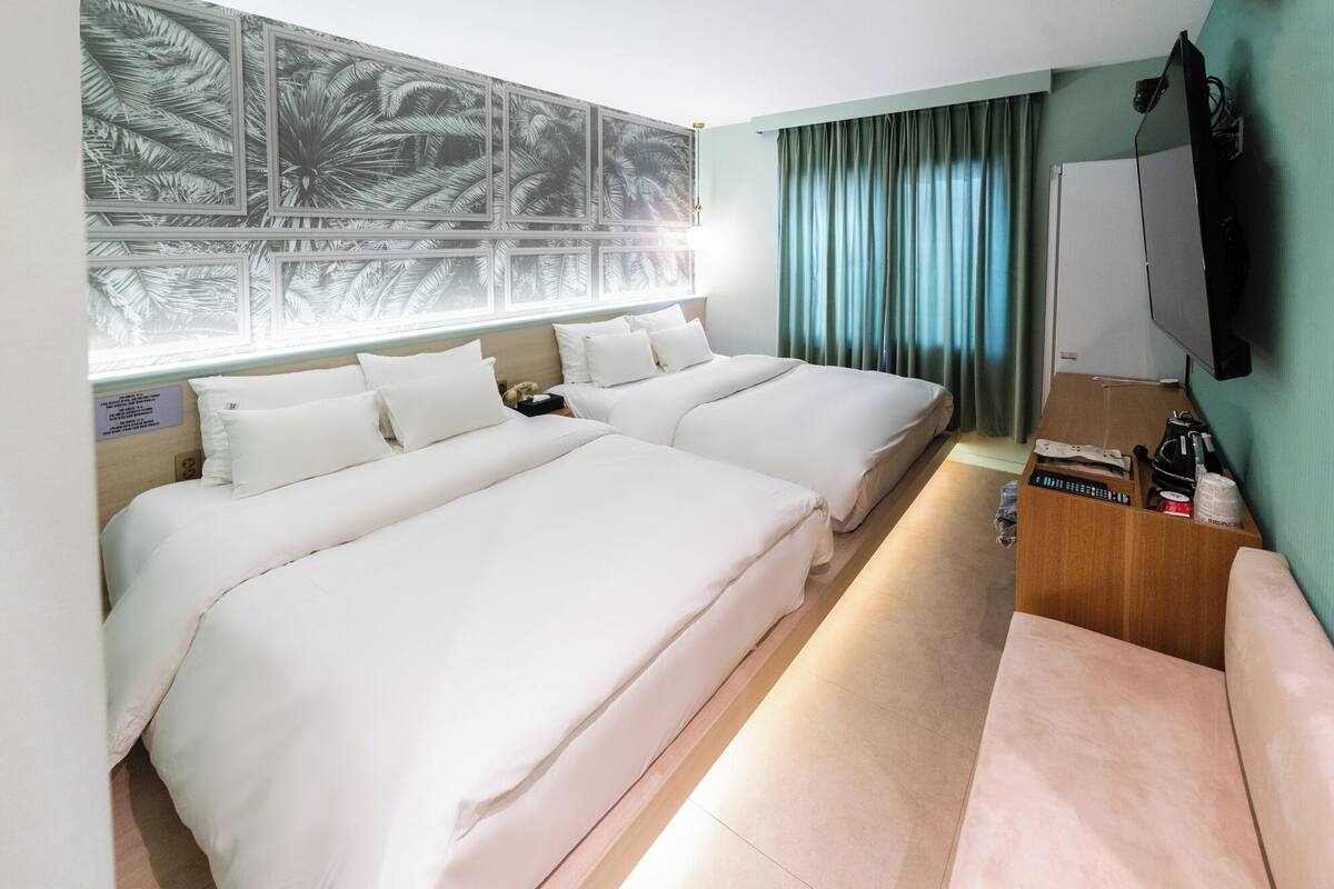 Habitación de hotel con dos camas, un televisor, una mesita de noche de madera y una ventana con cortinas.