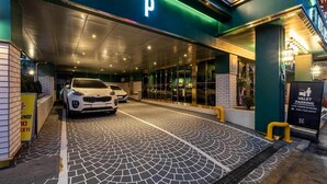 A valet parking area with a white car parked inside, a 'P' sign above the entrance, and a signboard indicating valet parking services. - WONJU Hotel Ippda (Wonju)
