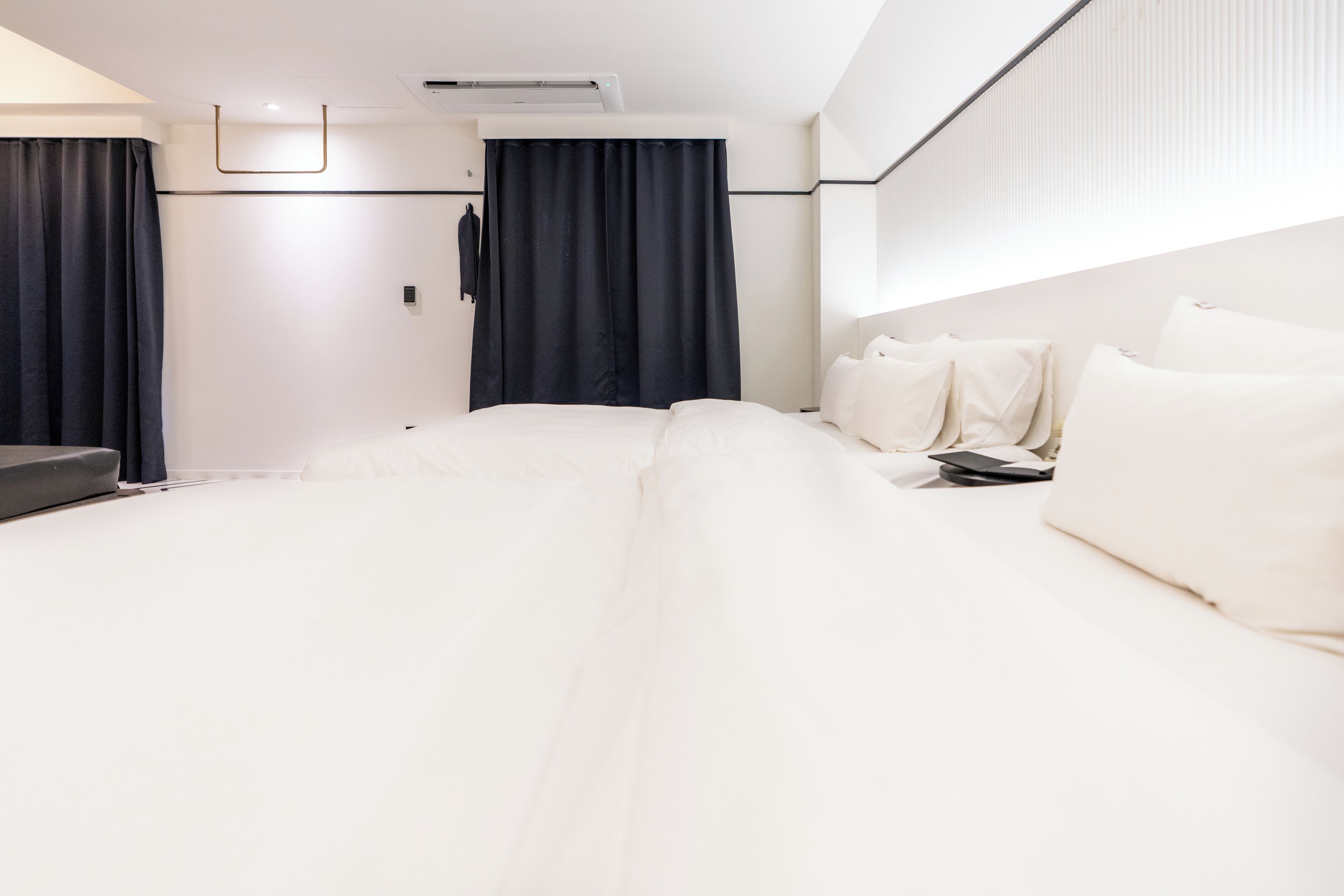Una habitación de hotel moderna con una cama grande, una mesita de noche, un televisor de pantalla plana y un ventanal con cortinas.