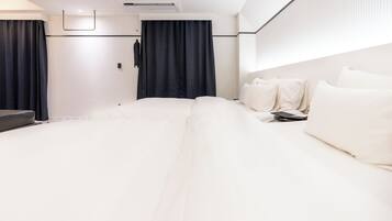 Una habitación de hotel moderna con una cama grande, una mesita de noche, un televisor de pantalla plana y un ventanal con cortinas.
