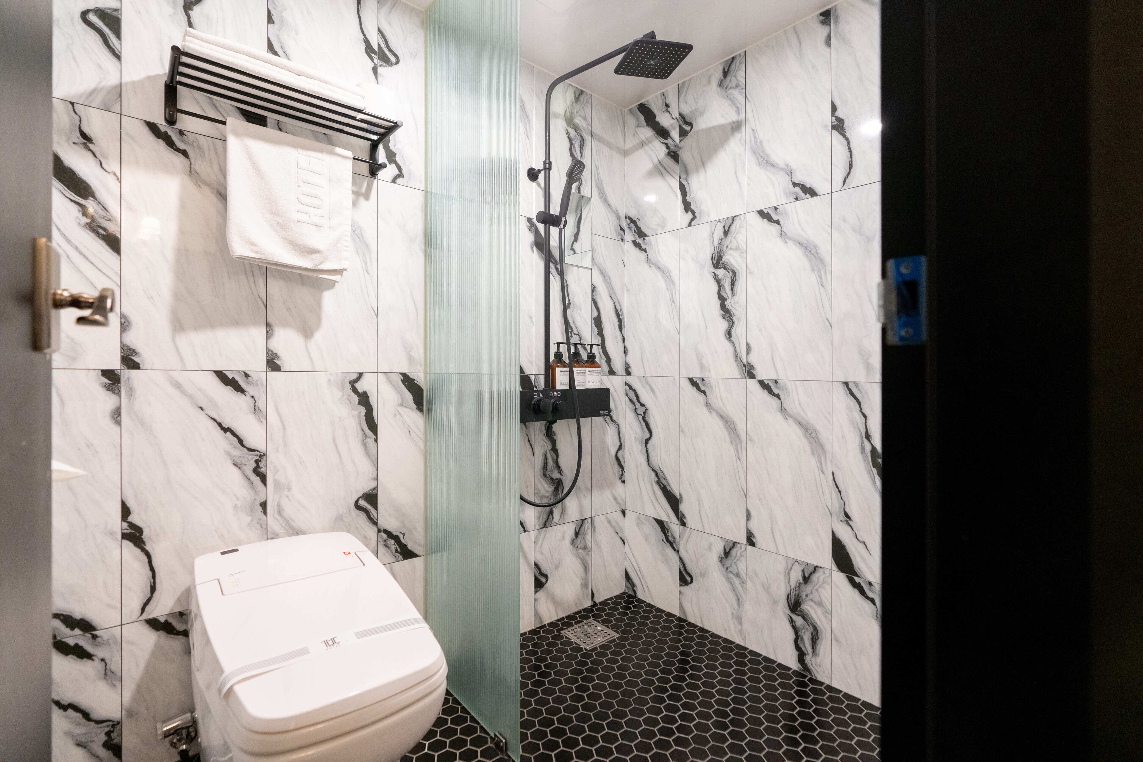 Un baño con inodoro, ducha y perchero para toallas.