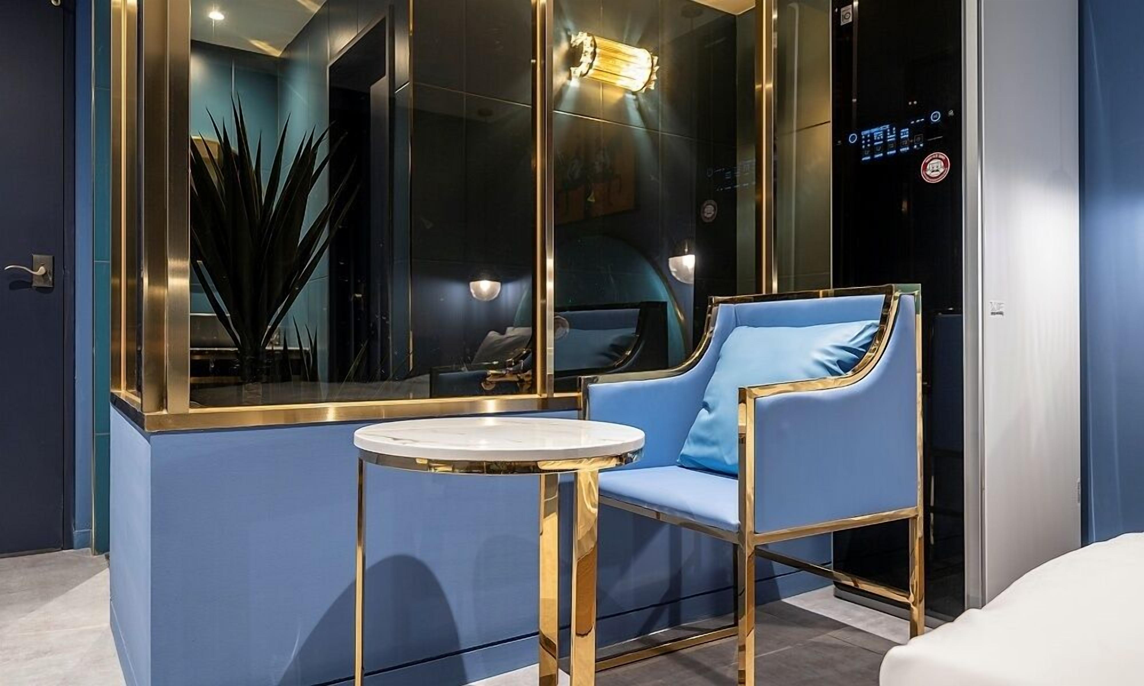 A modern room with a blue chair, a small round table, and a large mirror reflecting the room's interior.