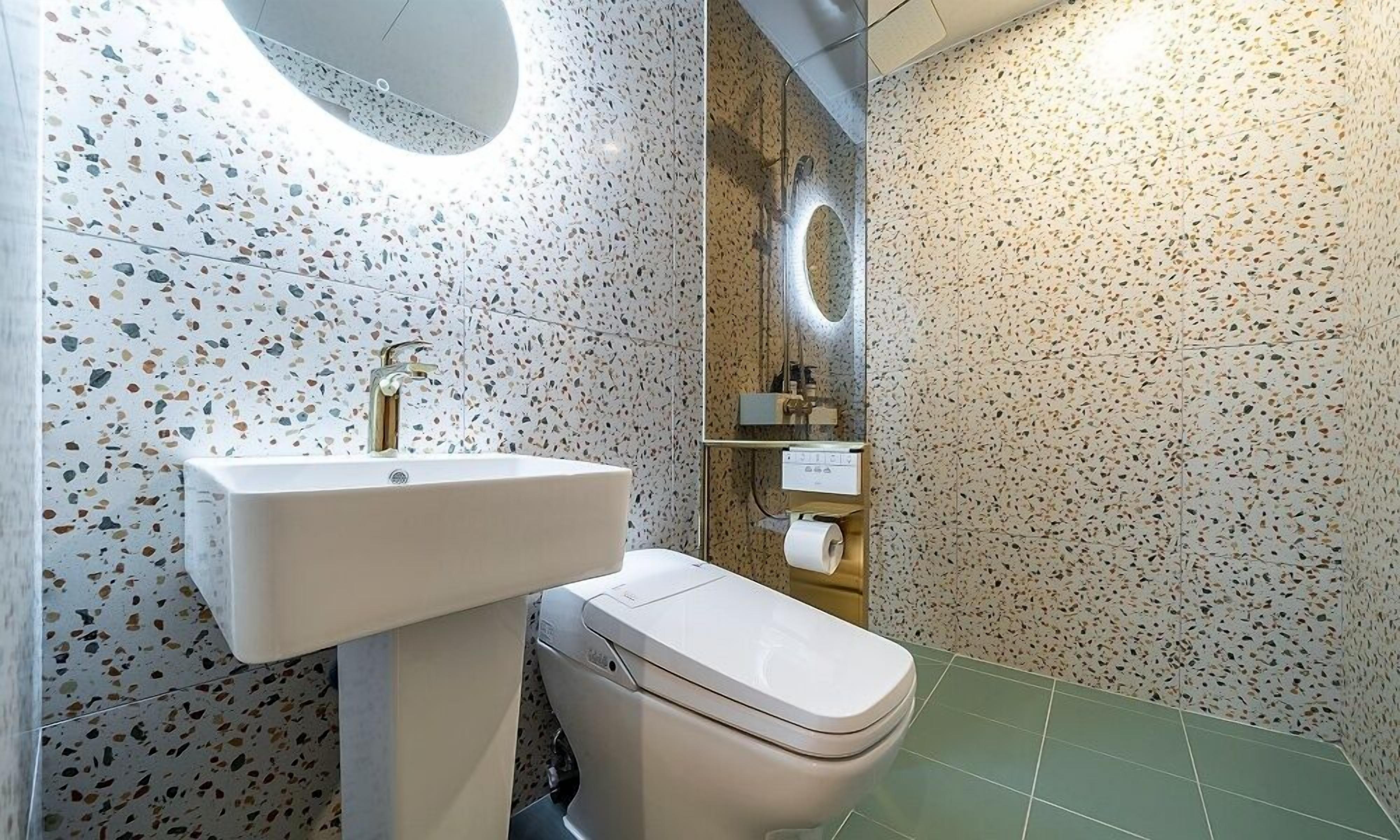A bathroom with a white sink, a toilet, and a mirror. The walls are covered with speckled tiles.