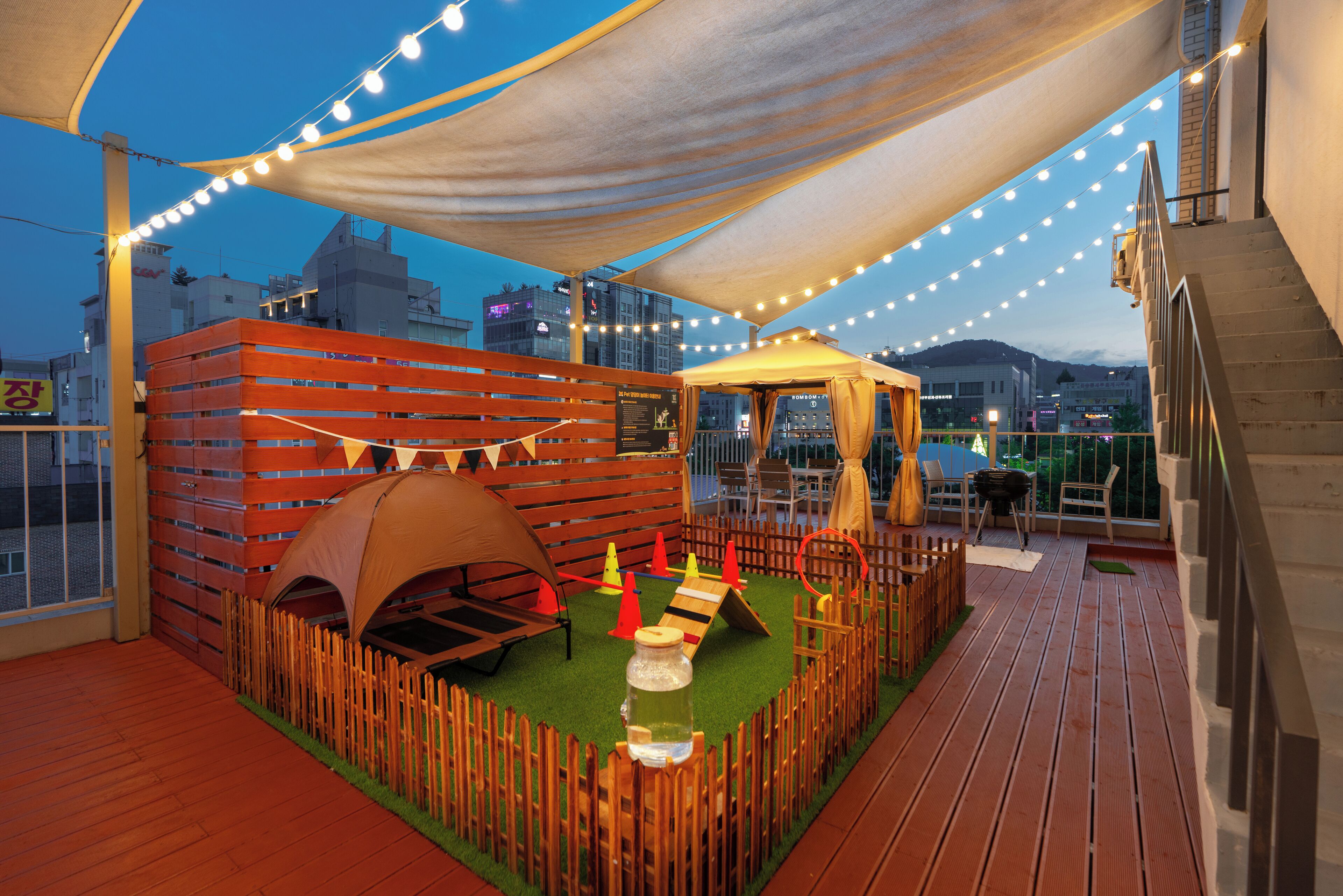 Terraza en la azotea con un área de juegos de madera, una tienda de campaña y luces colgantes.