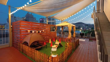 Terraza en la azotea con un área de juegos de madera, una tienda de campaña y luces colgantes.
