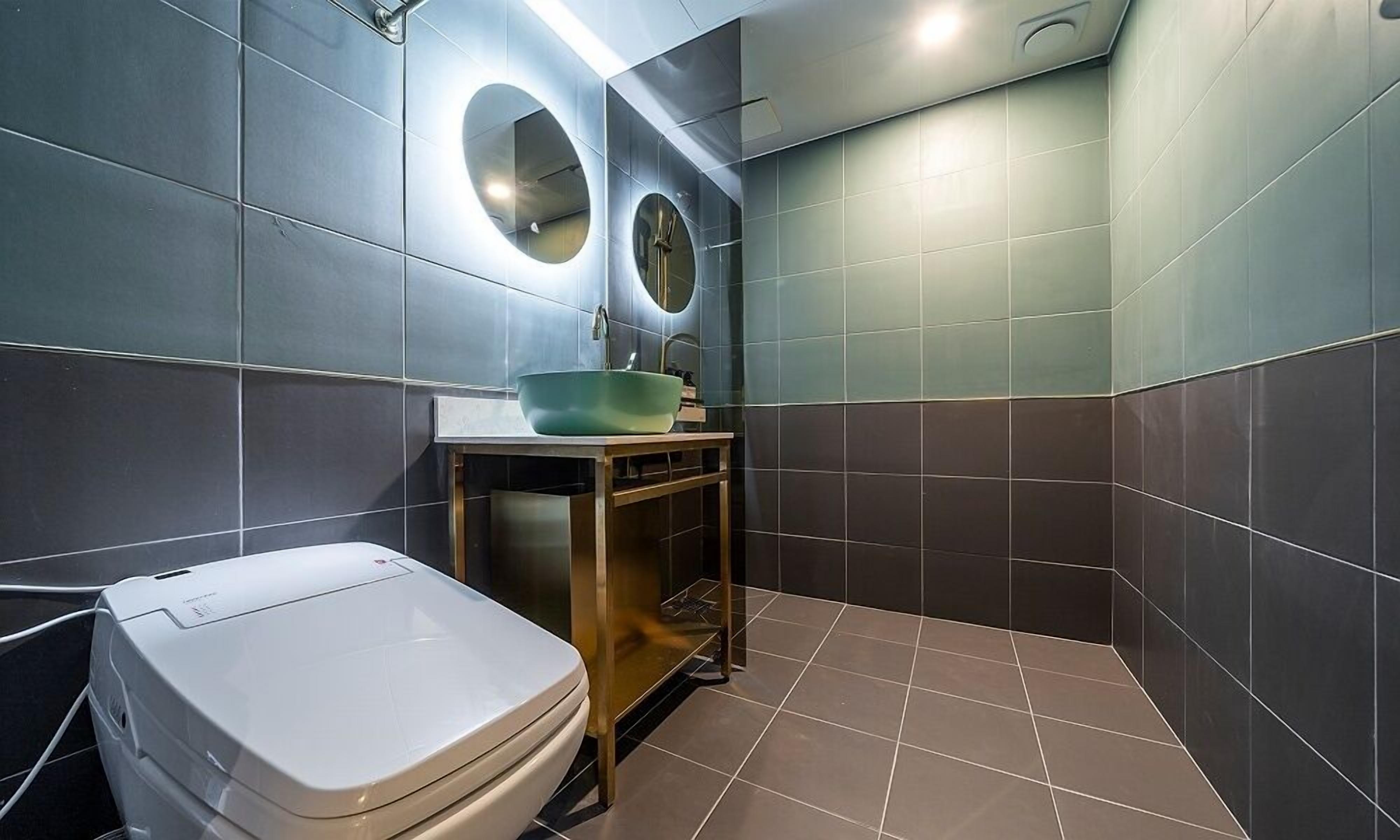 Un baño moderno con inodoro, lavamanos de color verde y dos espejos fijados a la pared.