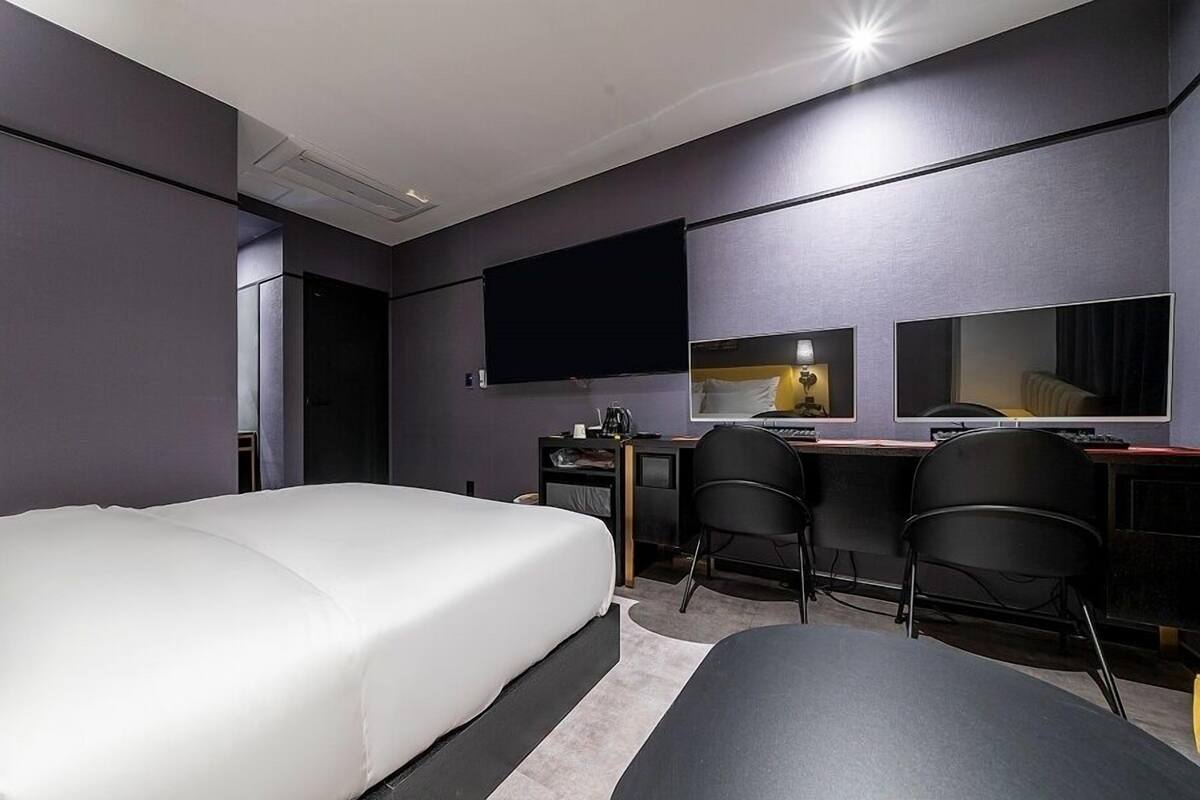 Una habitación de hotel moderna con una cama grande, un escritorio con dos sillas, un televisor de pantalla plana y un espejo amplio.
