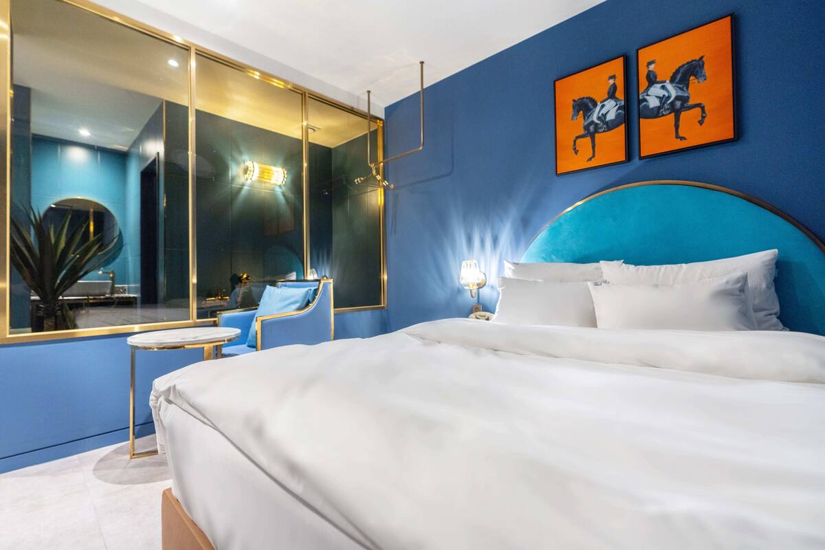 Una habitación de hotel moderna con una cama grande, una zona de estar con una silla, una mesita y un espejo amplio.