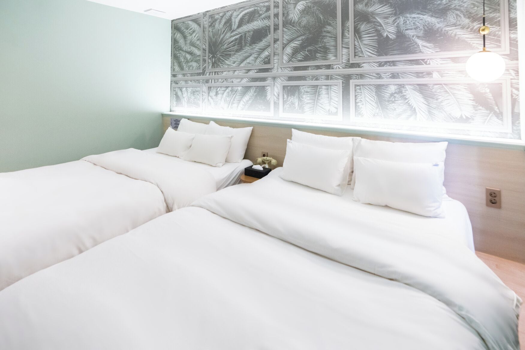 A double bed with white bedding, a nightstand with a lamp, and a wall with a leaf pattern.