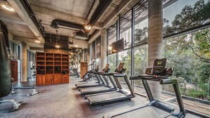 A gym with treadmills aligned along a wall with large windows, a wooden bench area, and visible exercise equipment.