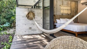 A bedroom with a bed, a hammock, a wall-mounted decor, and a view of greenery outside.
