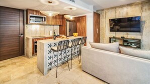 A modern kitchen with a central island, bar stools, a built-in oven, and a flat-screen TV mounted on the wall.