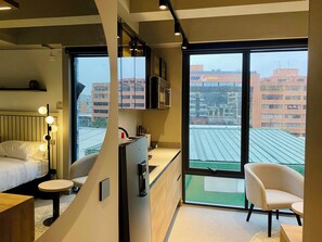 A modern hotel room with a bed, a desk, a chair, a large window, and a view of the cityscape. - Wynwood House 100 (Bogotá)