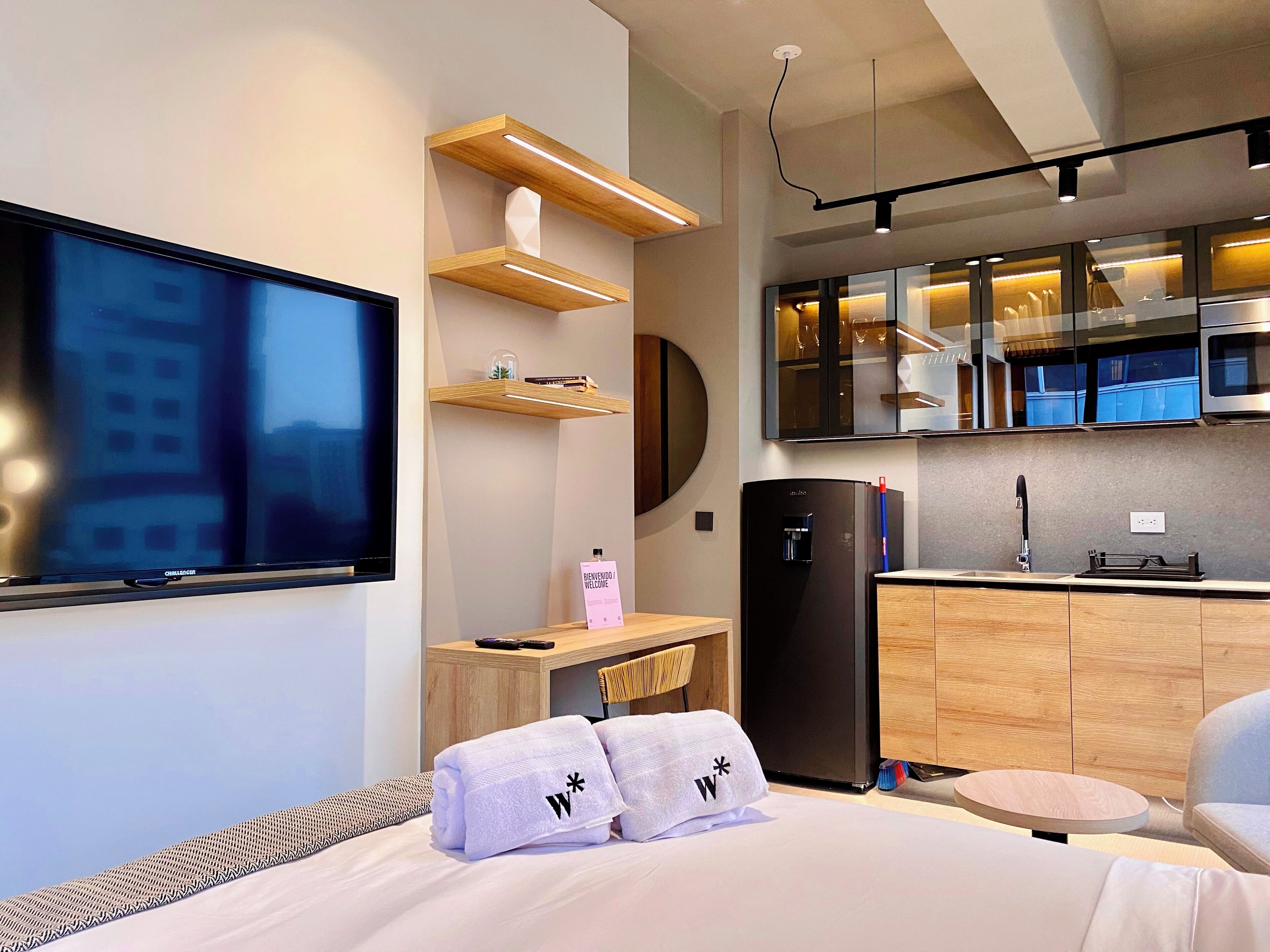 Une chambre d’hôtel moderne équipée d’un lit, d’une télévision, d’un bureau, d’un coin cuisine et d’une salle de bain.