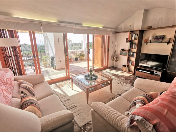 A living room with a sofa, coffee table, TV, bookshelf, and a balcony with potted plants. - Very cosy apartment with view in Las Ramblas Golf (VC)